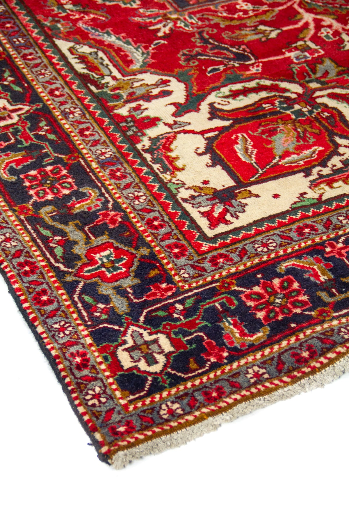 Vista en ángulo de alfombra oriental con campo rojo, elementos decorativos marfil y borde geométrico en azul y rojo.