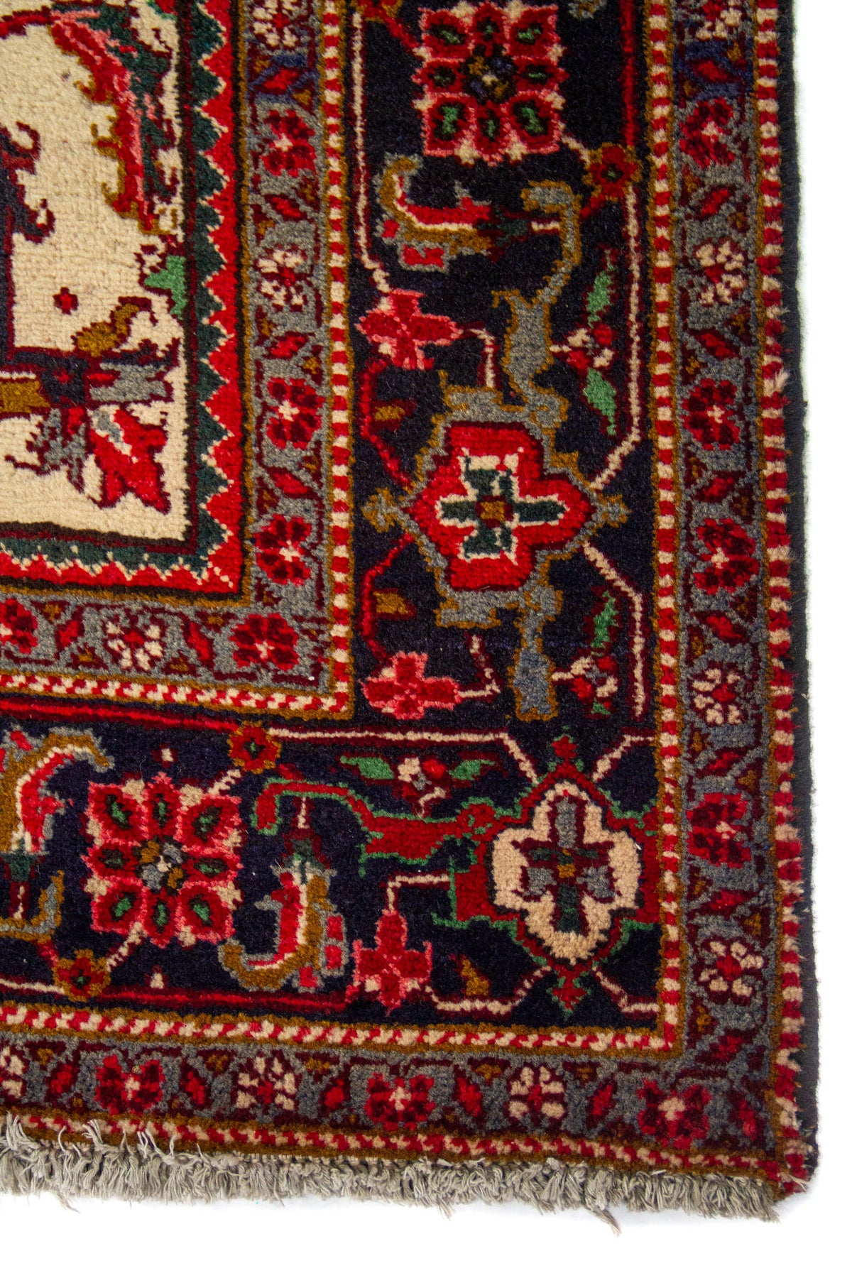 Primer plano de esquina de alfombra clásica con guarda azul oscuro, flores geométricas y flecos beige en el extremo.