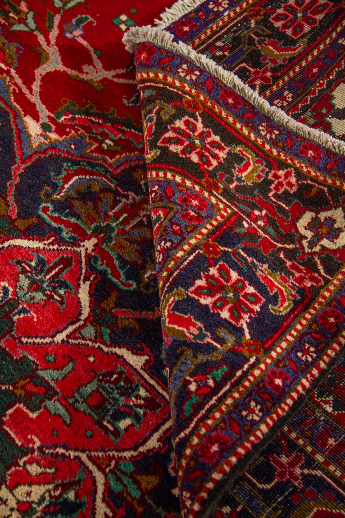 Alfombra doblada mostrando la flexibilidad del tejido, el contraste entre el fondo rojo y la guarda azul, y sus detalles ornamentales.