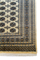 Alfombra Persa Bukara beige de 2.88 x 3.68 mts, detalle de esquina, guarda y flecos; se observan medallones ovalados repetidos y guardas geométricas