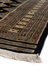 Alfombra Persa Bukara Yamouth negro de 2.03 x 3.10 mts, vista en perspectiva del campo oscuro y el borde; se observan rombos claros repetidos sobre campo oscuro y guarda ornamental