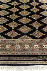 Alfombra Persa Bukara Yamouth negro de 2.03 x 3.10 mts, detalle de campo, flecos y guarda; se observan rombos claros repetidos sobre campo oscuro y guarda ornamental