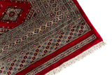 Alfombra Persa Bukara Yamouth rojo de 2.49 x 3.07 mts, vista en perspectiva del campo y la guarda; se observan retícula de rombos y motivos geométricos repetidos