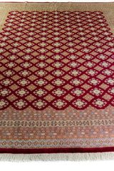Alfombra Persa Bukara Yamouth bordó de 2.50 x 3.00 mts, vista en perspectiva del campo y la guarda; se observan retícula geométrica sobre campo oscuro y guardas claras