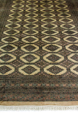 Alfombra Persa Bukara Yamouth marrón y beige de 2.20 x 3.05 mts, vista en perspectiva del campo oscuro y la guarda; se observan motivos alargados y rombos repetidos sobre campo oscuro