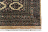 Alfombra Persa Bukara Yamouth marrón y beige de 2.20 x 3.05 mts, detalle de borde y flecos; se observan motivos alargados y rombos repetidos sobre campo oscuro