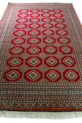 Alfombra Persa Bukara Yamouth rojo de 3.00 x 2.00 mts, vista en perspectiva del campo rojo y la guarda; se observan medallones geométricos repetidos y guardas ornamentales