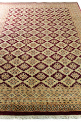 Alfombra Persa Bukara Yamouth beige de 1.88 x 2.60 mts, vista en perspectiva del campo y la guarda; se observan entramado geométrico rojizo sobre campo claro