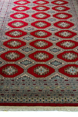 Alfombra Persa Bukara Yamouth rojo de 1.90 x 2.90 mts, vista en perspectiva del campo y la guarda; se observan medallones ovalados repetidos y guardas de varios niveles