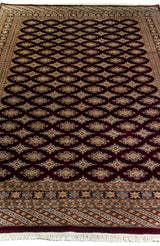 Alfombra Persa Bukara Yamouth bordó de 1.88 x 2.75 mts, vista en perspectiva del campo y las guardas; se observan entramado geométrico oscuro y guardas claras