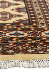 Alfombra Persa Bukara Yamouth beige de 1.88 x 2.90 mts, detalle de borde, flecos y motivos; se observan retícula geométrica con detalles de color en las guardas