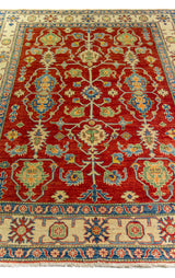 Alfombra Caucasica Kazak rojo de 1.80 x 2.60 mts, vista en perspectiva de la composición floral y el borde; se observan flores, hojas y enredaderas visibles dentro de una composición tradicional