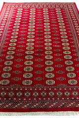 Alfombra Persa Bukara rojo de 1.85 x 2.75 mts, vista en perspectiva del campo rojo y la guarda; se observan columnas de medallones ovalados y guardas geométricas