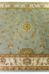 Alfombra Persa Isfahan celeste de 1.85 x 2.82 mts, vista en perspectiva del campo celeste; se observan motivos florales y vegetales de tono suave con guardas claras
