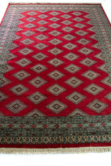 Alfombra Persa Yamouth rojo de 1.81 x 2.87 mts, vista en perspectiva del campo rojo y la guarda; se observan medallones y rombos repetidos en una trama geométrica
