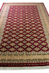 Alfombra Persa Yamouth rojo de 1.83 x 2.87 mts, vista en perspectiva del campo y la guarda; se observan retícula geométrica sobre campo intenso y guarda clara