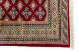 Alfombra Persa Yamouth rojo de 1.88 x 2.87 mts, detalle de esquina y guarda geométrica; se observan retícula geométrica de motivos repetidos y guardas múltiples
