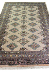 Alfombra Persa Yamouth beige de 1.55 x 2.44 mts, vista en perspectiva del campo y la guarda oscura; se observan motivos geométricos alargados y guardas oscuras