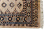 Alfombra Persa Yamouth beige de 1.55 x 2.44 mts, detalle de guarda y flecos; se observan pequeños motivos geométricos repetidos y guardas sobrias