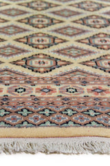 Alfombra Persa Yamouth beige de 1.55 x 2.54 mts, detalle de guarda y flecos; se observan rombos repetidos y guardas geométricas de contraste