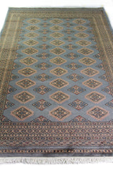 Alfombra Persa Yamouth celeste de 1.55 x 2.48 mts, vista en perspectiva del campo azul grisáceo; se observan rombos repetidos y guardas geométricas