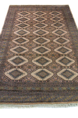 Alfombra Persa Yamouth marrón y beige de 1.52 x 2.44 mts, vista en perspectiva del campo marrón grisáceo; se observan grandes rombos claros y guardas oscuras