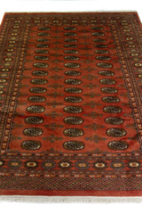 Alfombra Persa Yamouth marrón y naranja de 1.55 x 2.31 mts, vista en perspectiva del campo naranja tostado y la guarda; se observan medallones ovalados oscuros y guardas marrones