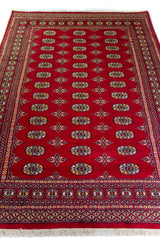 Alfombra Persa Bukara Yamouth rojo de 2.40 x 1.55 mts, vista en perspectiva del campo y las guardas; el diseño muestra hileras de medallones ovalados sobre un campo rojo y guardas geométricas densas