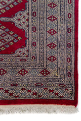 Alfombra Persa Bukara Yamouth rojo de 1.22 x 1.93 mts, vista en perspectiva del campo y las guardas; el diseño muestra una retícula vertical de medallones enlazados y guardas geométricas finas