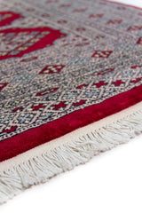 Alfombra Persa Bukara Yamouth rojo de 1.22 x 1.93 mts, detalle de guarda, borde y textura; el diseño muestra una retícula vertical de medallones enlazados y guardas geométricas finas