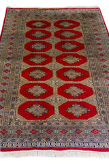 Alfombra Persa Bukara Yamouth rojo de 1.27 x 2.00 mts, detalle de guarda, borde y textura; el diseño muestra medallones geométricos repetidos en dos columnas y un marco ornamental de alto contraste