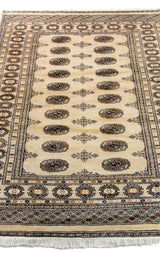 Alfombra Persa Bukara Yamouth beige de 1.24 x 1.73 mts, vista en perspectiva del campo y las guardas; el diseño muestra medallones ovalados oscuros alineados sobre un campo claro y guardas geométricas profundas