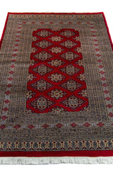 Alfombra Persa Yamouth rojo de 1.28 x 1.90 mts, vista en perspectiva del campo y las guardas; el diseño muestra una cadena de medallones romboidales enlazados y guardas geométricas compactas