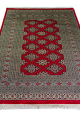 Alfombra Persa Yamouth rojo de 1.28 x 1.90 mts, detalle de guarda, borde y textura; el diseño muestra una cadena de medallones romboidales enlazados y guardas geométricas compactas