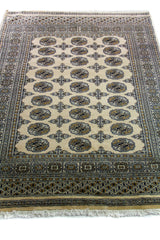 Alfombra Persa Bukara Yamouth beige de 1.27 x 1.80 mts, vista en perspectiva del campo y las guardas; el diseño muestra una secuencia ordenada de medallones oscuros sobre fondo beige con borde profundo