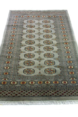 Alfombra Persa Bukara Yamouth celeste de 1.25 x 1.90 mts, vista en perspectiva del campo y las guardas; el diseño muestra medallones ovalados y pequeños acentos geométricos sobre un campo celeste grisáceo