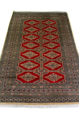 Alfombra Persa Yamouth beige y rojo de 1.20 x 1.97 mts, vista en perspectiva del campo y las guardas; el diseño muestra medallones romboidales rojos enlazados sobre un campo beige y guardas oscuras