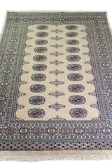 Alfombra Persa Bukara Yamouth beige de 1.37 x 1.83 mts, vista en perspectiva del campo y las guardas; el diseño muestra medallones ovalados oscuros sobre un campo beige con múltiples guardas geométricas