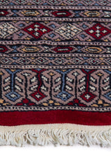 Alfombra Persa Yamouth rojo de 1.24 x 1.68 mts, detalle de guarda, borde y textura; el diseño muestra medallones enlazados rojos sobre un campo claro con guardas geométricas azuladas
