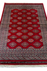 Alfombra Persa Yamouth rojo de 1.27 x 1.88 mts, vista en perspectiva del campo y las guardas; el diseño muestra una retícula de rombos rojos enlazados con guardas geométricas de alto contraste