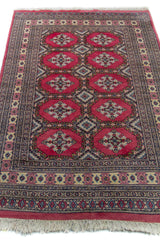 Alfombra Persa Yamouth rosa de 1.28 x 1.88 mts, vista en perspectiva del campo y las guardas; el diseño muestra medallones rosados repetidos sobre un campo oscuro y un borde ornamental detallado
