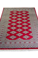 Alfombra Persa Yamouth rojo de 1.24 x 1.78 mts, vista en perspectiva del campo y las guardas; el diseño muestra una cadena de rombos rojos enlazados sobre un campo claro y guardas oscuras
