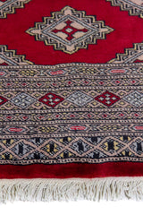 Alfombra Persa Yamouth rojo de 1.24 x 1.78 mts, detalle de guarda, borde y textura; el diseño muestra una cadena de rombos rojos enlazados sobre un campo claro y guardas oscuras