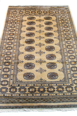 Alfombra Persa Bukara Yamouth beige de 1.27 x 1.86 mts, vista en perspectiva del campo y las guardas; el diseño muestra medallones ovalados oscuros sobre un campo beige y un marco geométrico bien definido