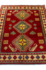 Alfombra Caucasica Kazak rojo y beige de 1.17 x 1.58 mts, vista en perspectiva del campo y las guardas; el diseño muestra tres grandes medallones geométricos sobre un campo rojo y guardas claras con pequeños acentos