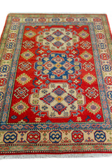 Alfombra Caucasica Kazak ladrillo con detalles multicolor de 1.24 x 1.78 mts, vista en perspectiva del campo y las guardas; el diseño muestra medallones y motivos geométricos de gran contraste distribuidos sobre un campo ladrillo con bordes multicolores