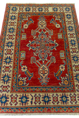 Alfombra Caucasica Kazak ladrillo y beige de 0.94 x 1.45 mts, vista en perspectiva del campo y las guardas; el diseño muestra un motivo central estilizado sobre un campo ladrillo enmarcado por guardas beige