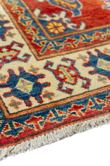 Alfombra Caucasica Kazak ladrillo y beige de 0.94 x 1.45 mts, detalle de guarda, borde y textura; el diseño muestra un motivo central estilizado sobre un campo ladrillo enmarcado por guardas beige