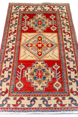 Alfombra Caucasica Kazak rojo y beige de 0.91 x 1.60 mts, vista en perspectiva del campo y las guardas; el diseño muestra tres medallones geométricos destacados sobre un campo rojo con amplias guardas beige