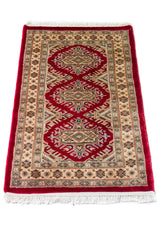 Alfombra Persa Yamouth beige y rojo de 0.61 x 1.09 mts, vista en perspectiva del campo y las guardas; el diseño muestra un motivo enlazado rojo de gran escala sobre un campo beige y un borde rojo intenso